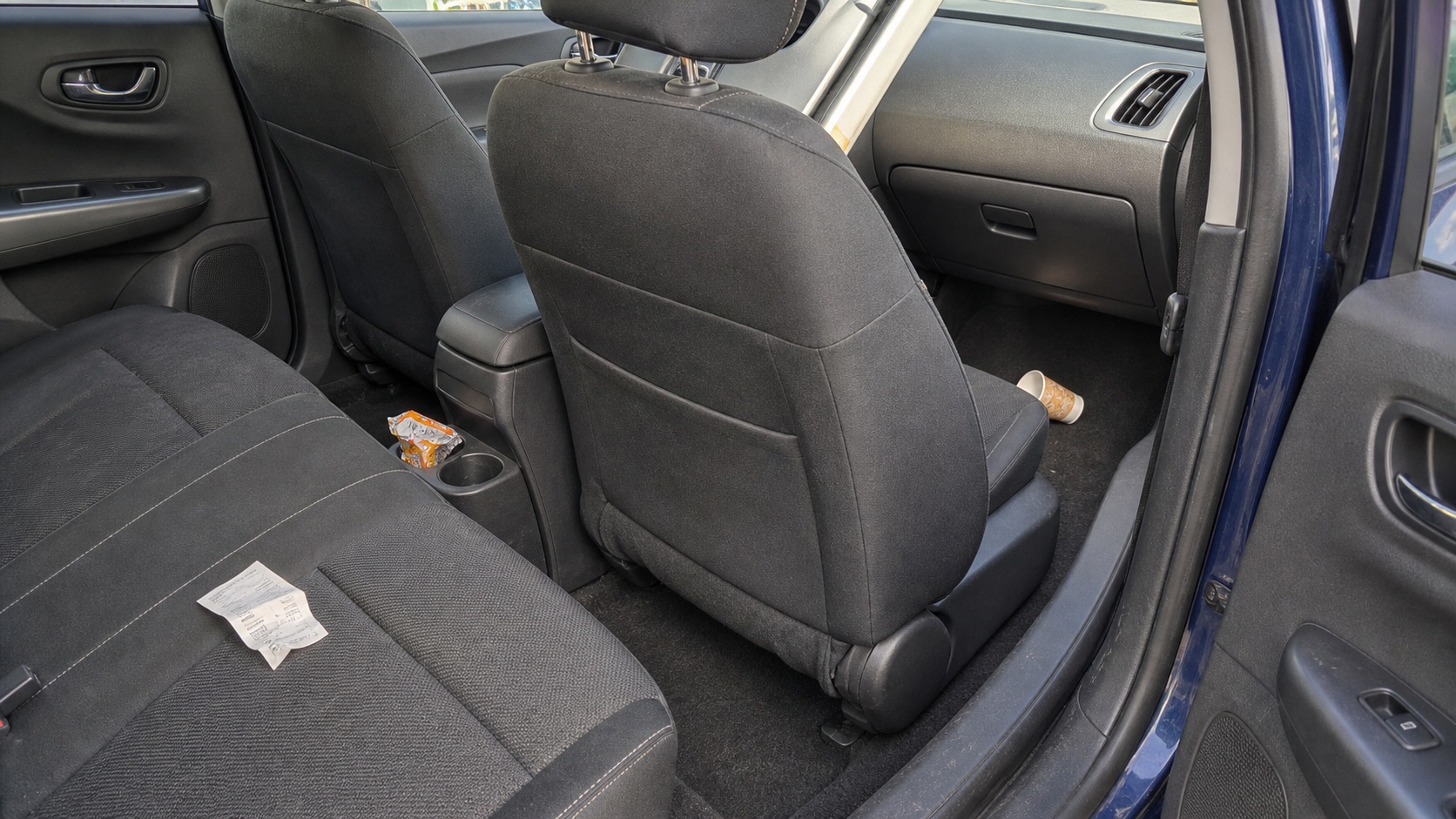 An ordinary compact car interior with a paper cup, wrapper, and receipt in separate passenger and floor zones, showing why placement matters before choosing a trash bin.