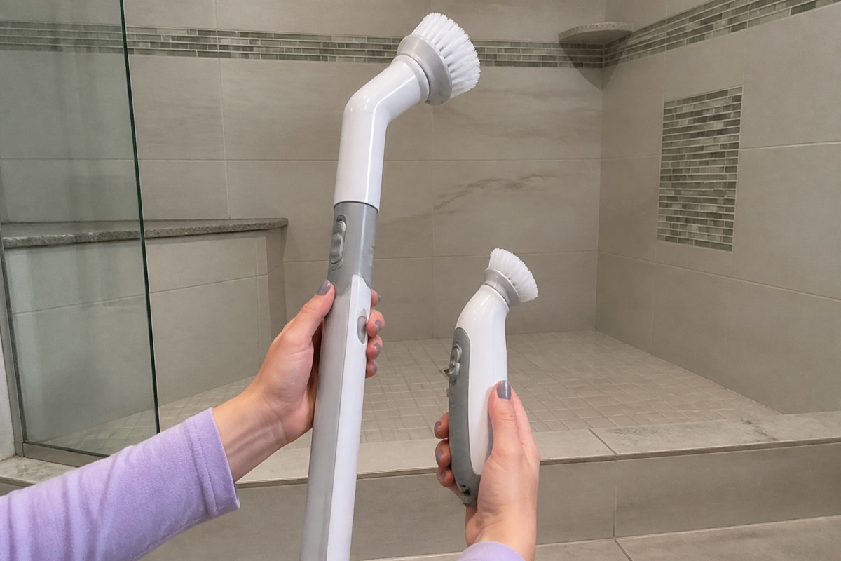 Hands compare an unbranded long-handle electric scrubber with a compact detail scrubber in a tiled shower.