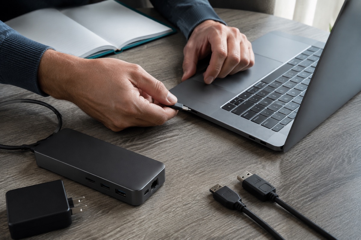 AI illustration of hands checking a USB-C connection beside a laptop, dock and charging equipment.