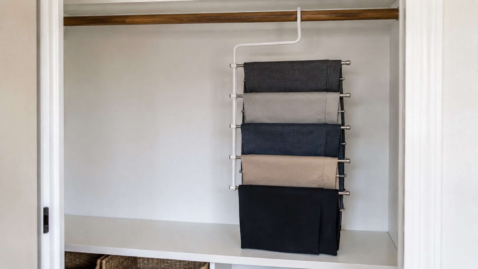 Five pairs of trousers on a vertical tiered hanger in a small closet with a shelf close below the lowest pair.