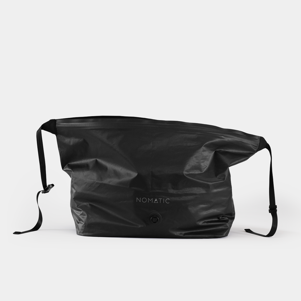 Black NOMATIC Vacuum Bag 2.0 shown compressed with its valve and adjustable straps visible.