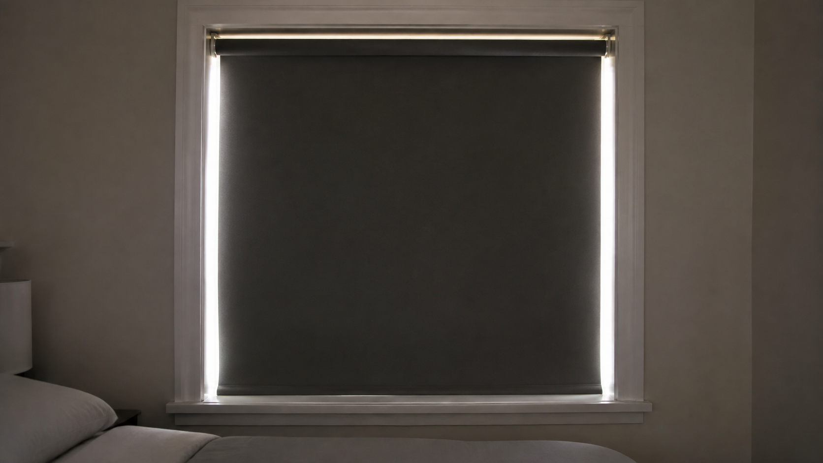 A dark roller shade blocks the center of a bedroom window while thin lines of morning light remain at the sides and top.
