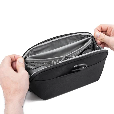 Hands hold the Black Peak Design Small Wash Pouch open, showing the divided interior and the hook stored in its outer pocket.