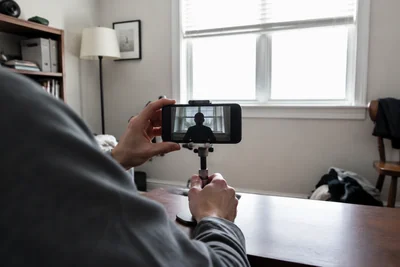 Over-the-shoulder view of a phone recording a dark silhouette against a bright window in a modest home office.