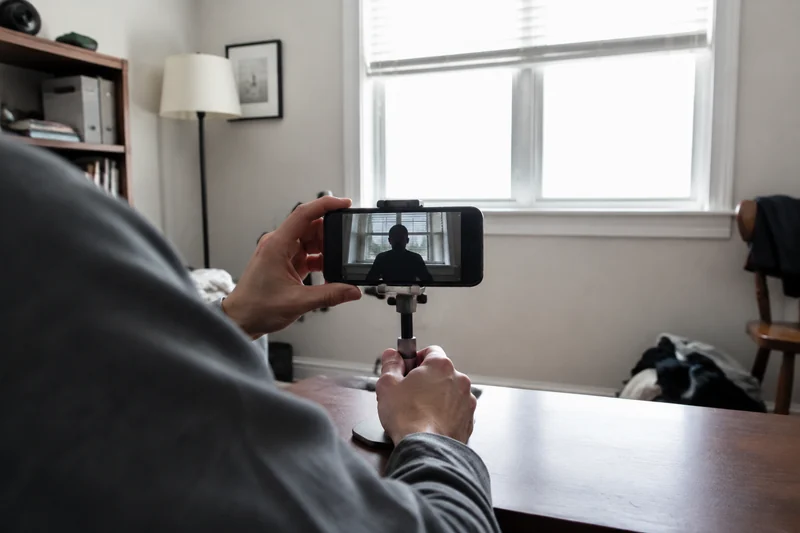 Over-the-shoulder view of a phone recording a dark silhouette against a bright window in a modest home office.