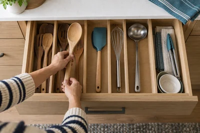 AI illustration of hands arranging long cooking utensils in a divided kitchen drawer.