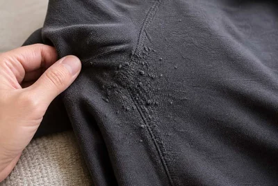 Hand inspecting fabric pills concentrated along a dark sweater seam.