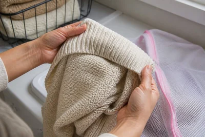 Hands turning a knit sweater inside out beside a mesh laundry bag.