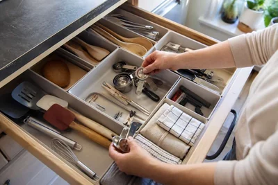 Hands sorting everyday cooking tools into useful zones inside a kitchen drawer.