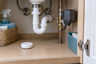 AI illustration of a floor leak detector and a separate pipe-mounted automatic shutoff device.