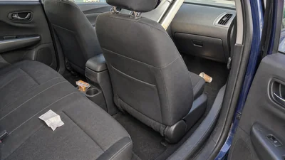 An ordinary compact car interior with a paper cup, wrapper, and receipt in separate passenger and floor zones, showing why placement matters before choosing a trash bin.