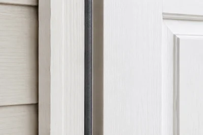 Close-up of a dark gray compression weatherstrip seated along a white exterior door jamb beside a slightly open white door.